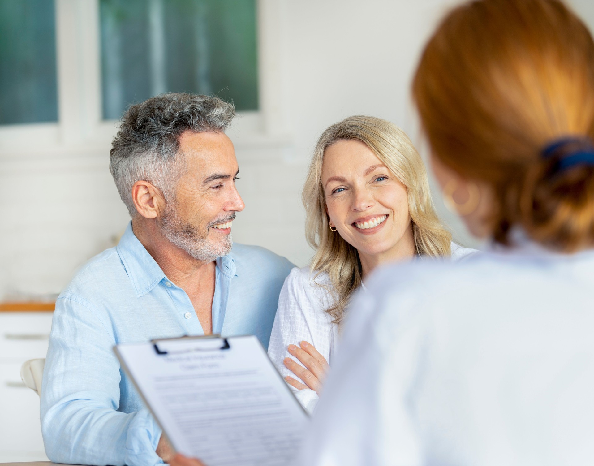 Doctor filling out medical insurance form with mature couple.